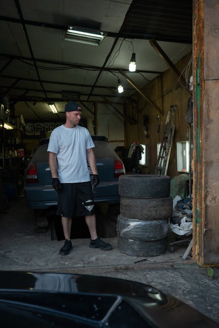 Mechanic in a garage workshop with car and tools around, focusing on a repair task.