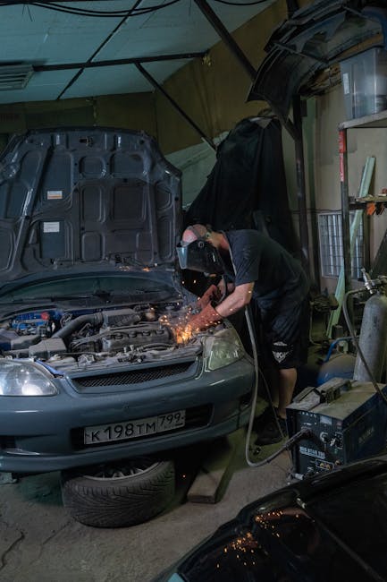 A mechanic with protective gear welding a car engine in a workshop setting, showcasing industrial repair.